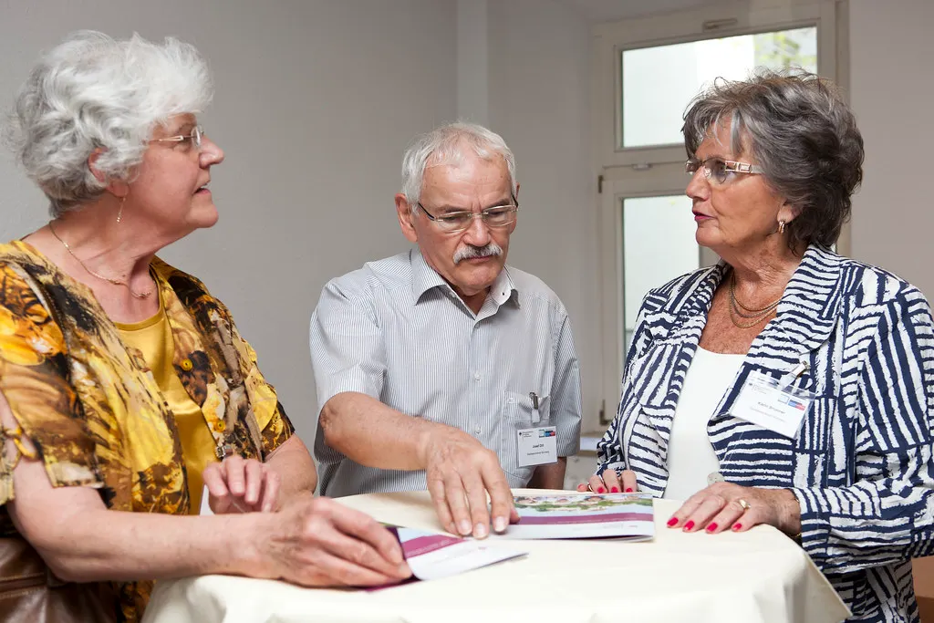 Three older people stand at a table looking over an information leaflet together.