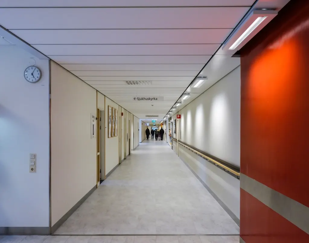A long, bright hospital corridor with a handrail and people walking in the distance.