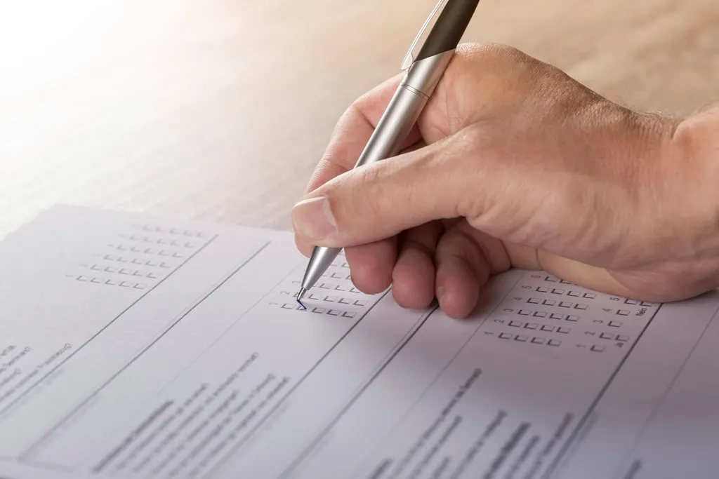 A hand with a pen ticking boxes on a paper form.