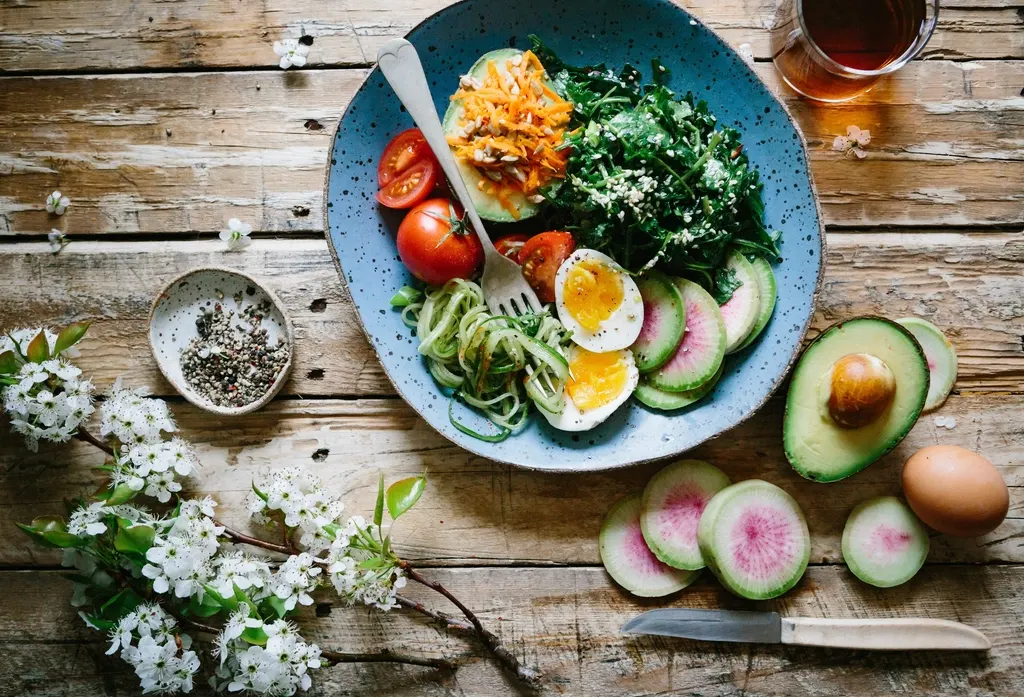 A colourful salad bowl with egg, tomatoes, greens and avocado on a wooden table.