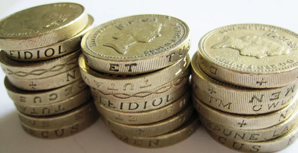 Three stacks of British one-pound coins on a white surface.