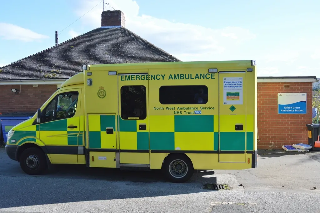A yellow and green North West Ambulance Service NHS ambulance parked at its station.