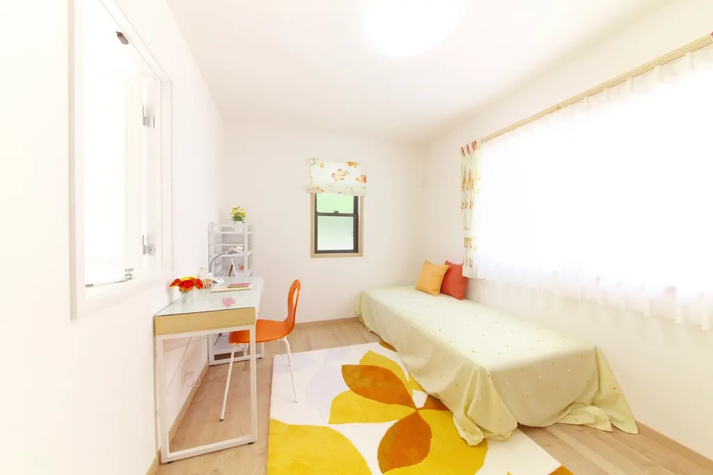 A bright, tidy bedroom with a single bed, desk, flowers and a yellow rug.