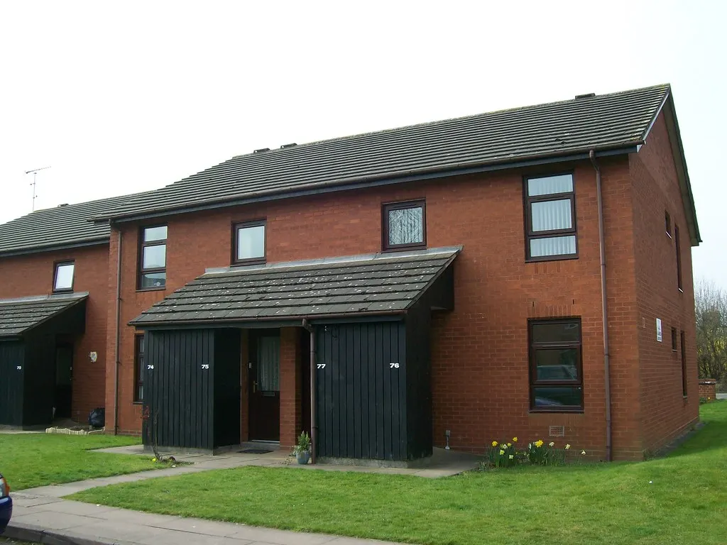 A two-storey red-brick block of sheltered housing flats with a neat front lawn.
